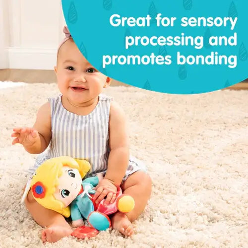 Baby holding a plush doll with yellow hair on a rug. A blue bubble highlights sensory processing and bonding benefits.