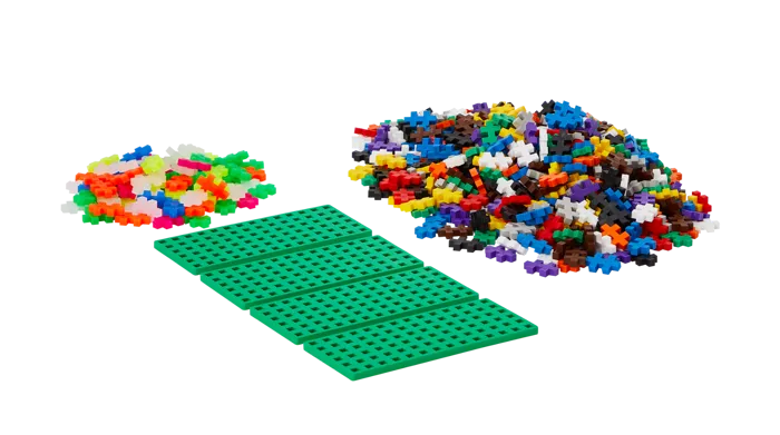 Four green baseplates and two piles of colorful cross-shaped interlocking building pieces on a white background.