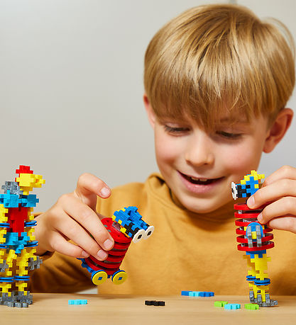 Smiling boy plays with colorful toy robots made from interlocking red, blue, and yellow building pieces.
