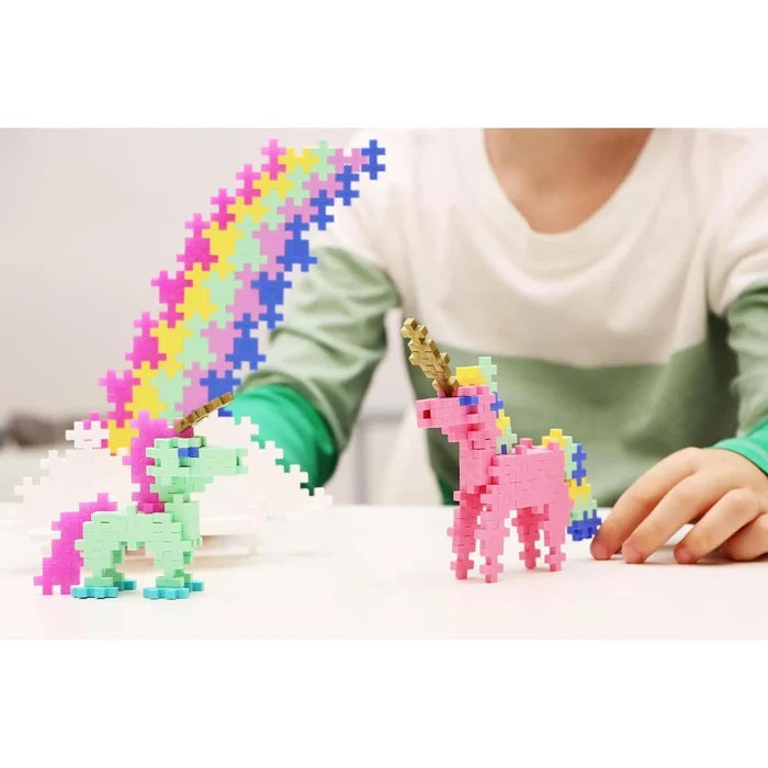 Two toy unicorns built from pink, mint, and rainbow cross-shaped interlocking blocks on a white table.