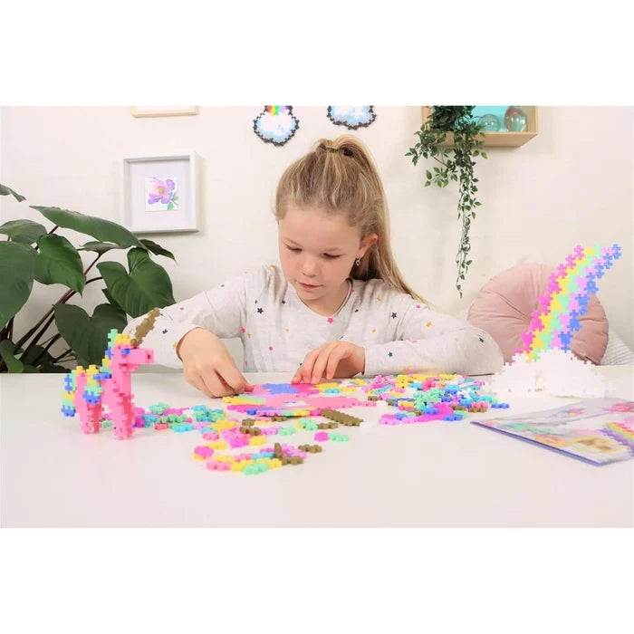 Young girl building with colorful cross-shaped blocks to create a pink unicorn and rainbow on a white table.
