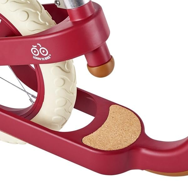 Close-up of a red balance bike with a cream patterned tire, cork footrest, and brown steering stop.