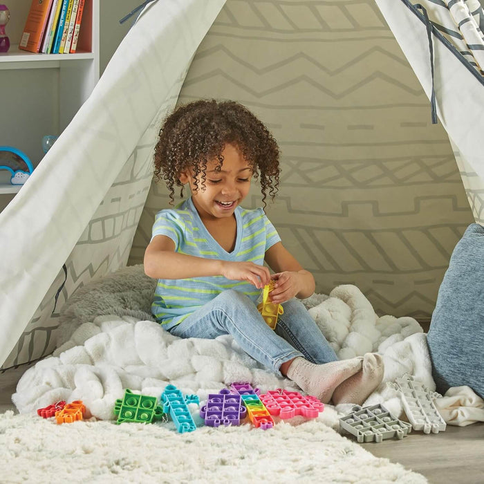 Child playing with colorful character-shaped silicone bubble poppers inside a cozy patterned teepee on a white rug.