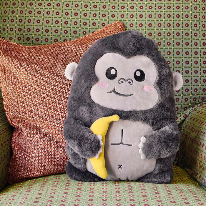 Soft grey plush gorilla with pink cheeks and a light grey belly holding a yellow banana on a patterned chair.