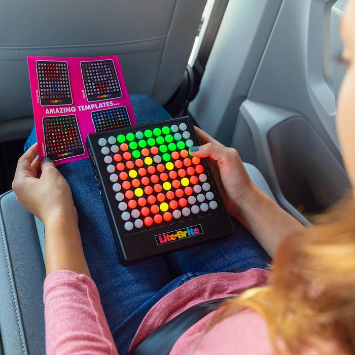 Handheld Lite Brite Touch with a grid of glowing colored buttons and a template sheet held by a person in a car.