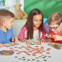 Three children playing with brown square tiles, character cards, a star wand, and a green sand timer on a table.
