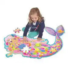 A young girl assembles a large, colorful mermaid floor puzzle with vibrant pink, blue, and yellow scales.