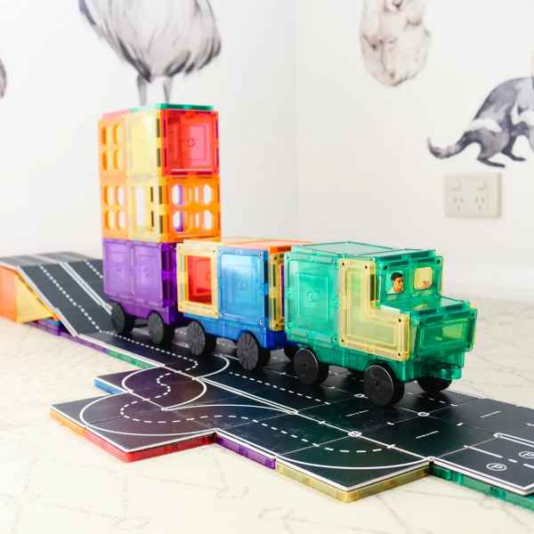 Colorful magnetic tile truck and train on black road toppers with white street markings.