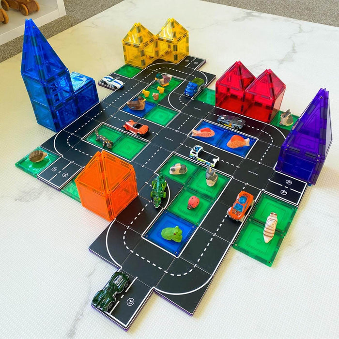 Black magnetic road toppers with white markings laid out on colorful tiles with toy cars and animal figurines.