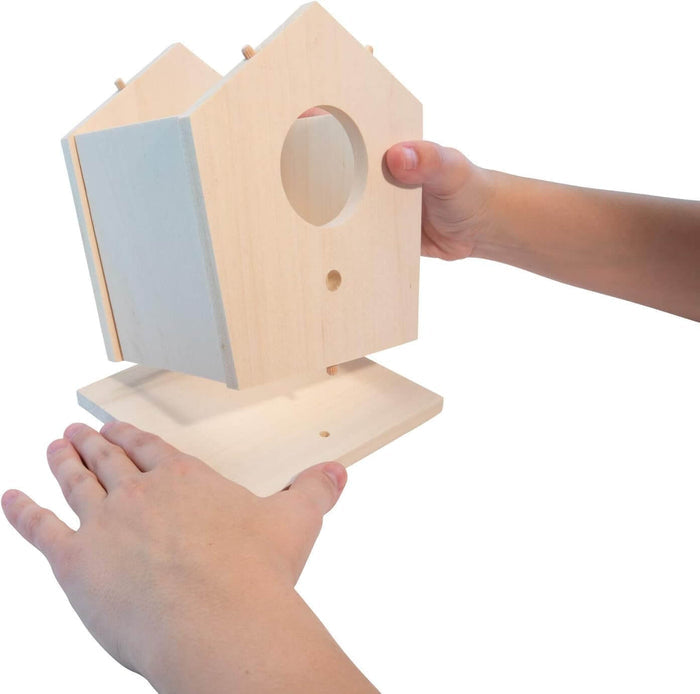 Hands holding an unfinished light wood birdhouse with a round entry hole and a separate flat base.