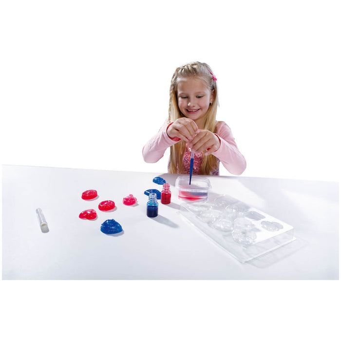 Young girl mixing colorful dyes to make red and blue soaps with a pipette and clear plastic mold tray.