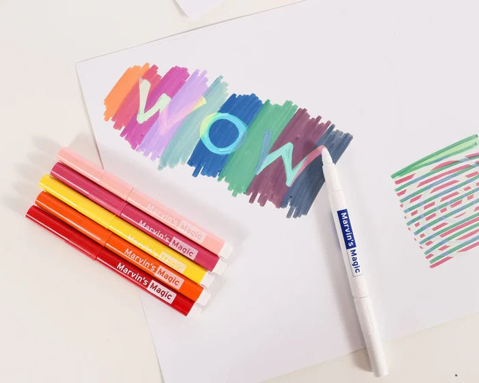 Five Marvin’s Magic markers and a white magic pen creating a color-changing WOW design on white paper.
