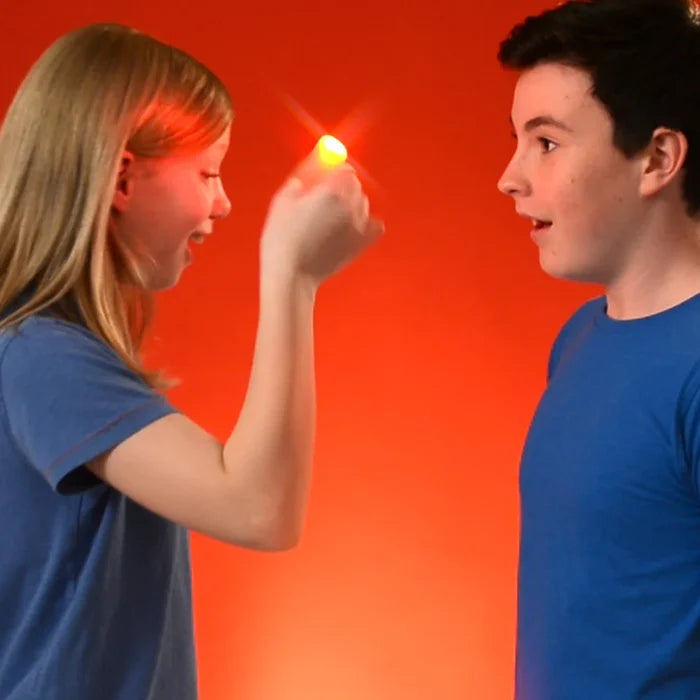 A girl holds a bright red glowing light at her fingertips while a boy watches in amazement against an orange background.