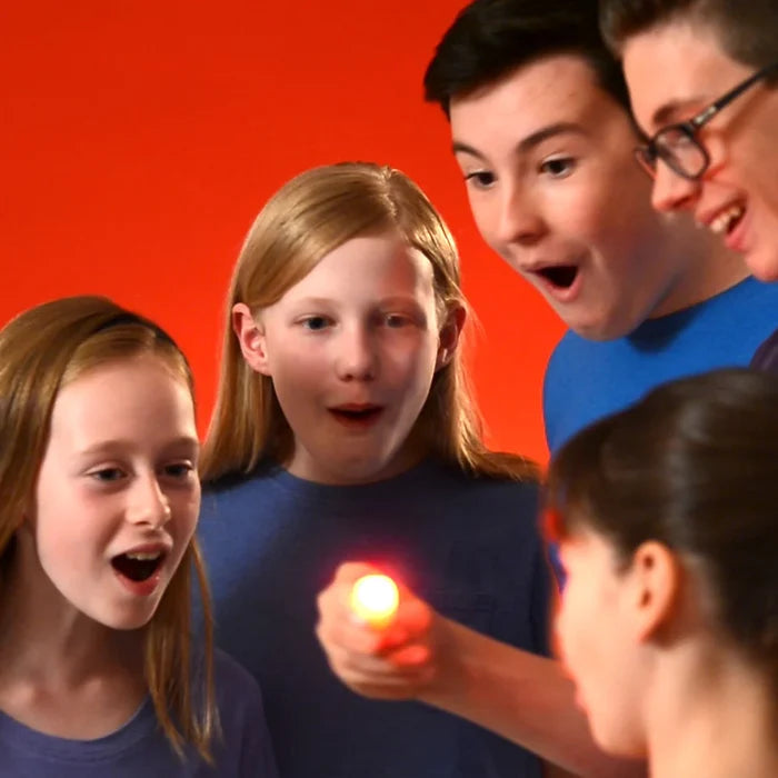 Surprised children look at a bright glowing point of light held by a hand against a solid red background.
