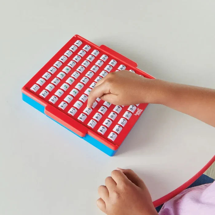 Child's hand presses a white button on a red and blue plastic board featuring rows of subtraction equations.