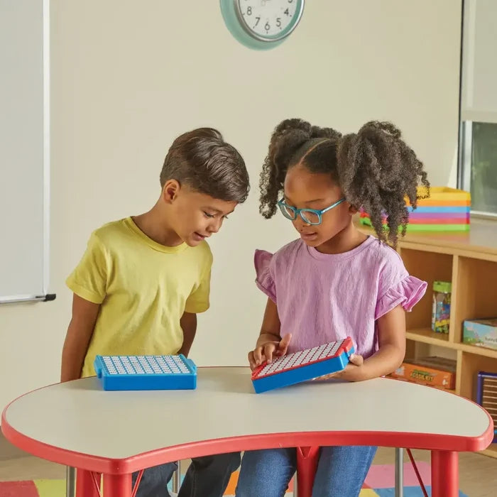 Two children using blue math fact boards with red sliding buttons at a kidney-shaped table in a classroom.