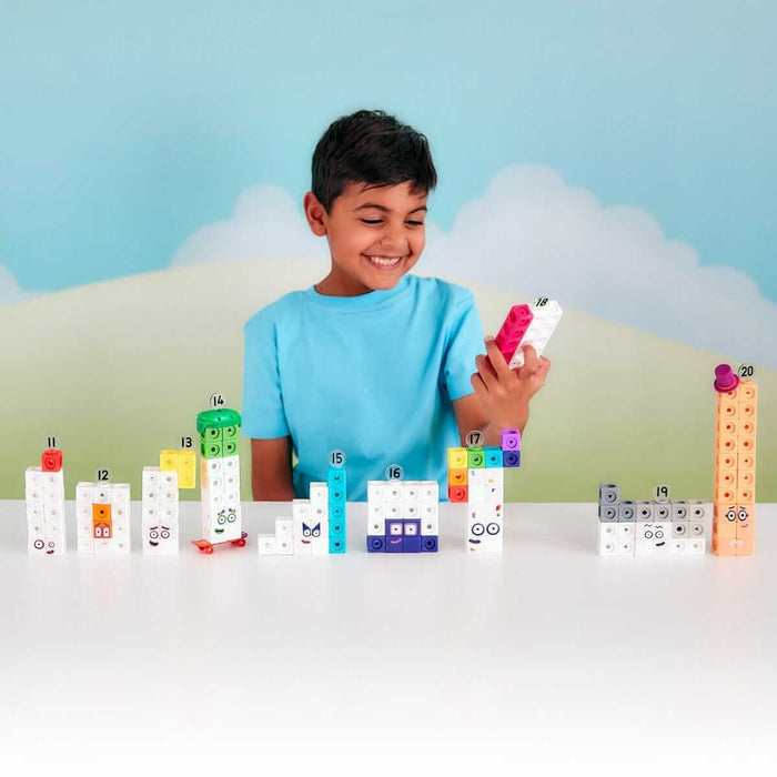 Smiling boy playing with colorful Numberblocks 11-20 figures made of interlocking MathLink cubes on a table.