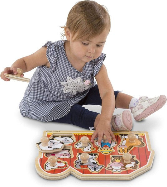 Toddler playing with a red barn-shaped wooden peg puzzle featuring animal pieces with easy-grasp knobs.