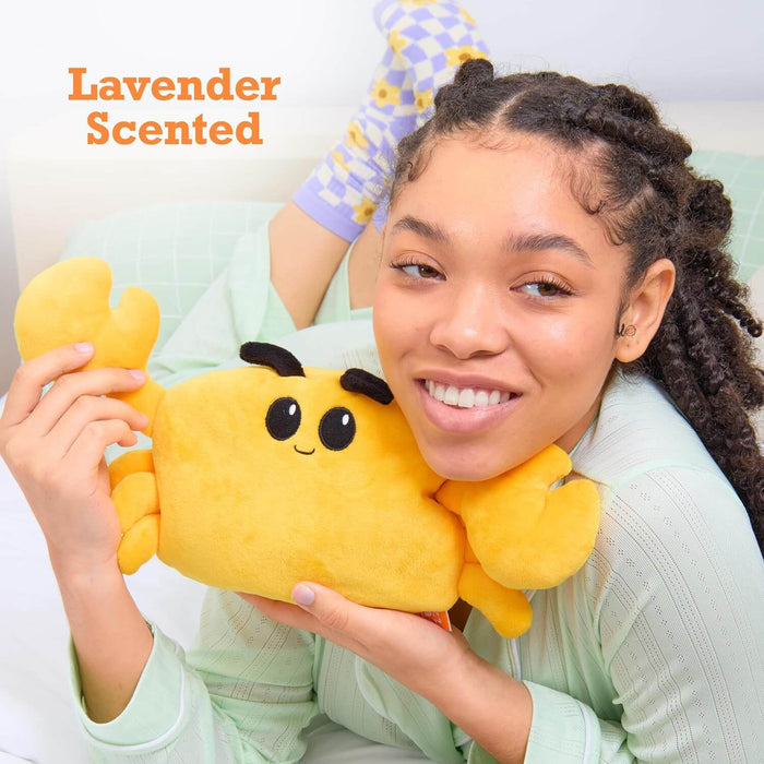 Smiling woman holds a yellow plush crab with black embroidered eyes. Orange text reads Lavender Scented.