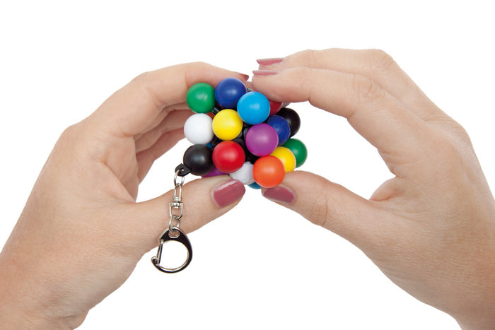 Hands holding a multicolored cube puzzle of connected spheres with a silver metal keychain.
