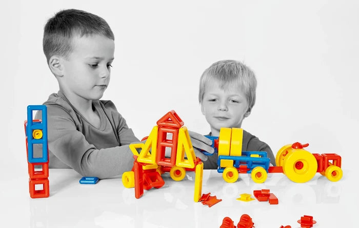Two boys build towers and vehicles using bright red, yellow, and blue geometric blocks and wheels.