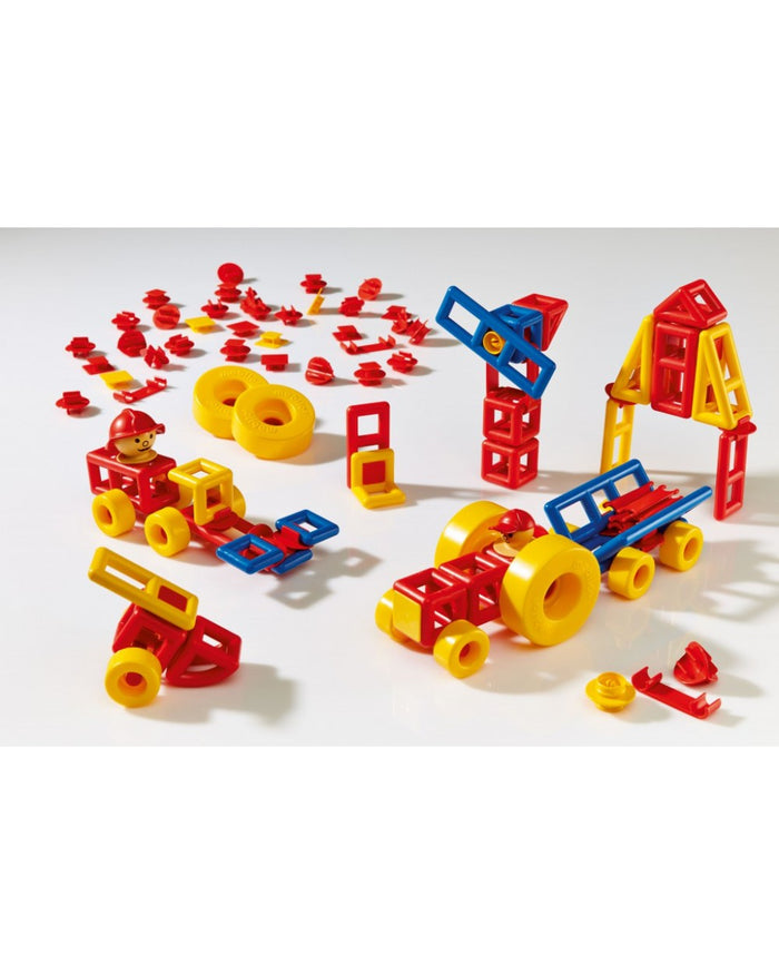 Red, blue, and yellow plastic building blocks and wheels assembled into toy trucks, a crane, and geometric structures.