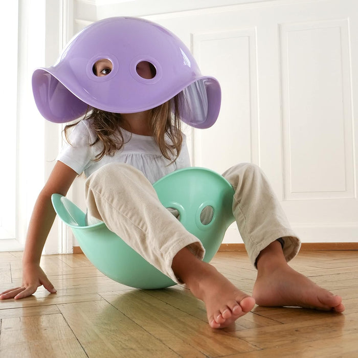 Child sitting in a mint green shell toy and wearing a purple shell toy with eye holes over their head as a mask.