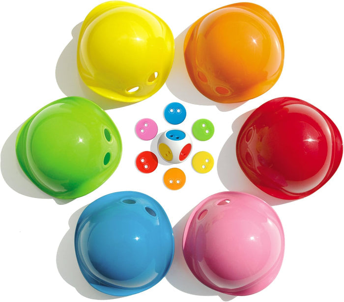 Six colorful bowl-shaped shells with holes arranged in a circle with a large die and matching chips in the center.
