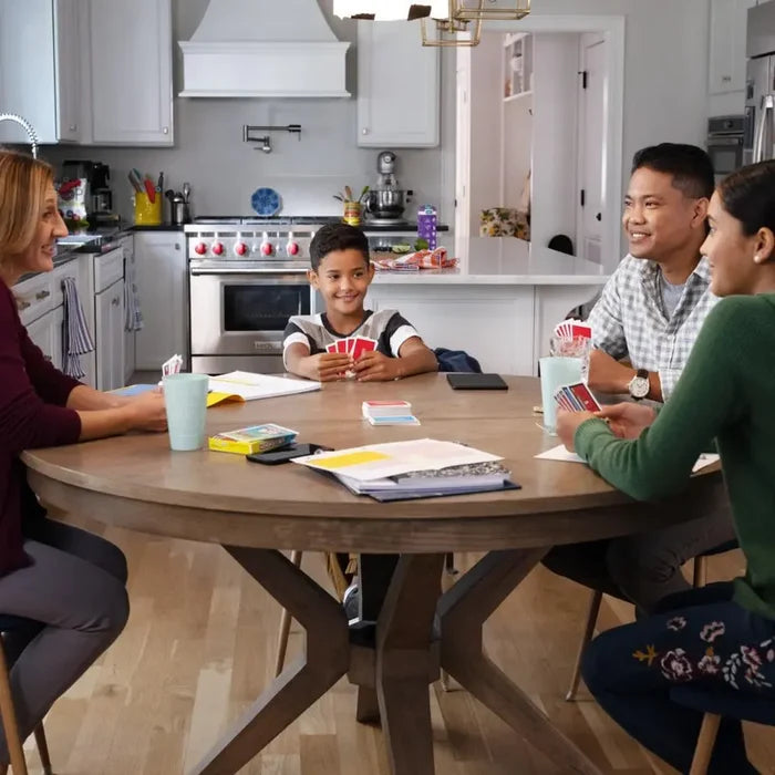 Family playing Monopoly Bid with red and blue cards and a yellow box around a round wooden table.