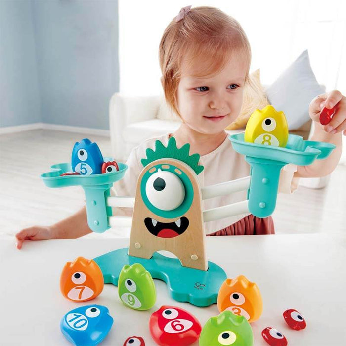 Child playing with a monster-shaped balance scale and colorful, numbered monster weights in various sizes.