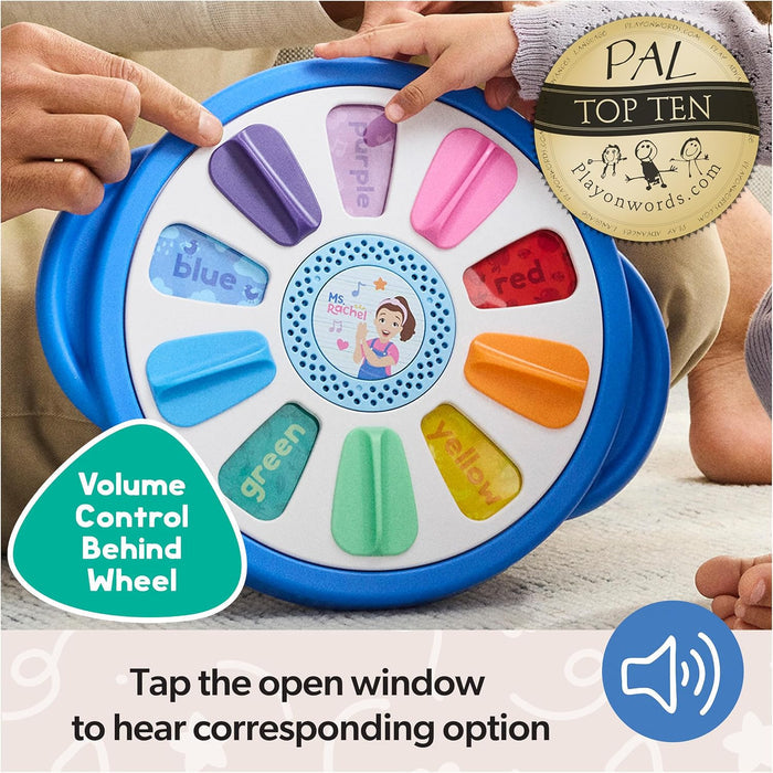 Blue toy wheel with colorful flip tabs and Ms. Rachel speaker being played with by a child and adult.