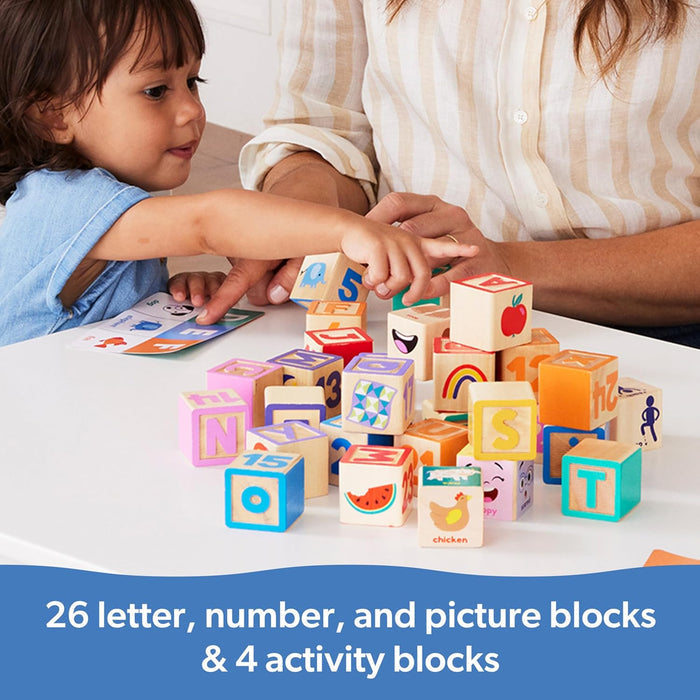 A child and adult playing with colorful wooden blocks featuring letters, numbers, and pictures on a white table.