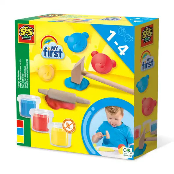 Yellow toy box showing blue, red, yellow dough tubs, wooden hammer and rolling pin, bear molds, and a toddler playing.