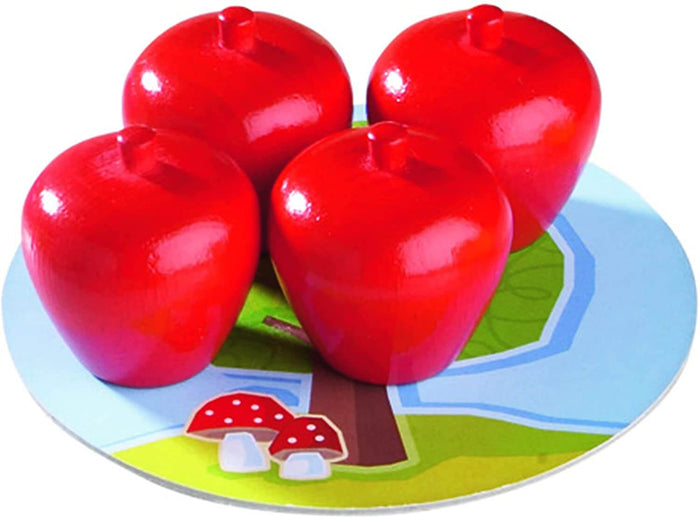 Four large, red wooden apple pieces on a circular game board illustrated with a tree and two red spotted mushrooms.