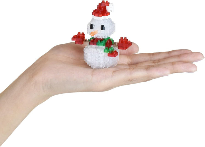 Miniature block snowman with red hat and green scarf held in a palm to show scale against a white background.