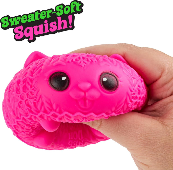 Hand squeezing a bright pink, round cat squishy with a knitted texture, large black eyes, and tiny pink ears.