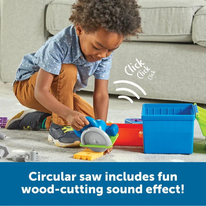 Young boy using a blue toy circular saw on yellow plastic wood. Part of a colorful tool set with a blue storage bin.