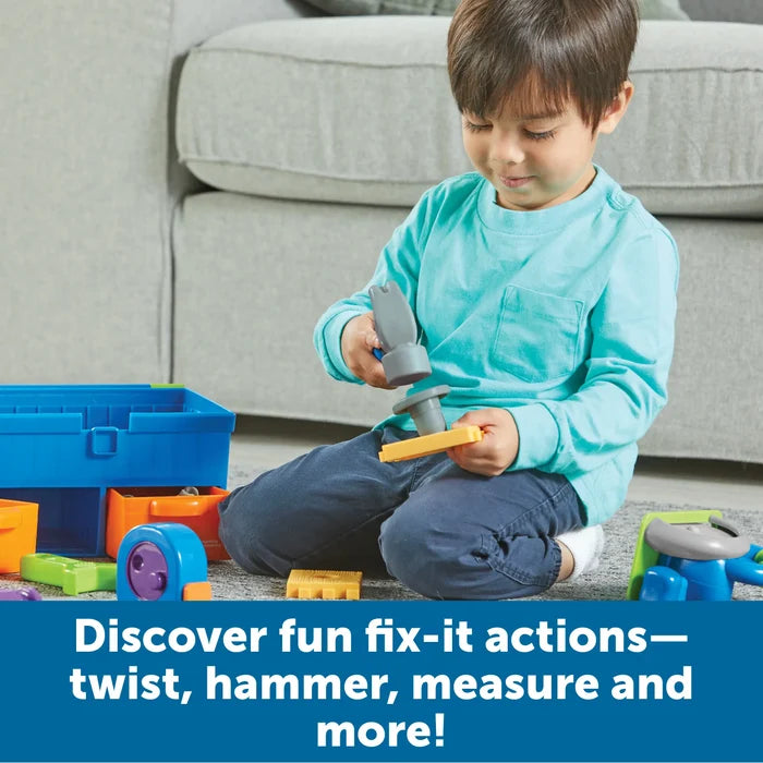 Child plays with a grey toy hammer and a blue toolbox with orange drawers and colorful plastic tools on the floor.