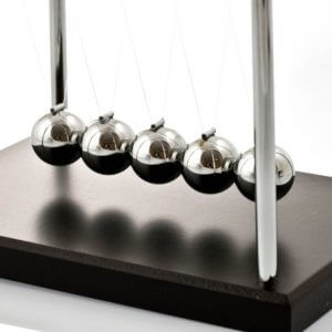 Five reflective chrome spheres suspended by thin strings on a silver metal frame with a dark wooden base.