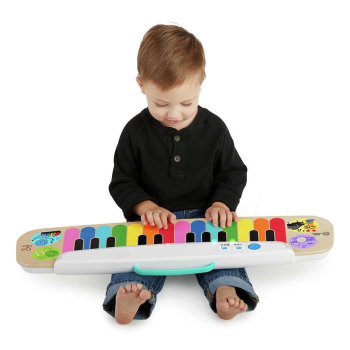 Toddler playing a wooden toy keyboard with vibrant rainbow-colored keys and a white control panel.