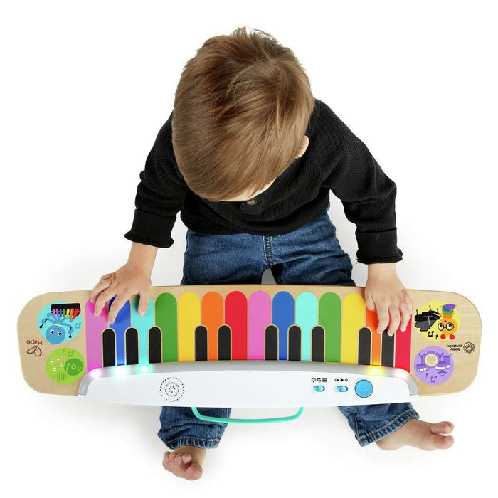 Overhead view of a child playing a colorful wooden touch piano with rainbow keys and animal illustrations.
