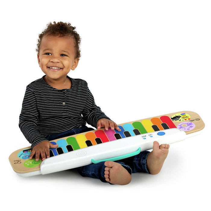 Toddler with a flat wooden toy keyboard featuring colorful rainbow keys and a white handle across their lap.