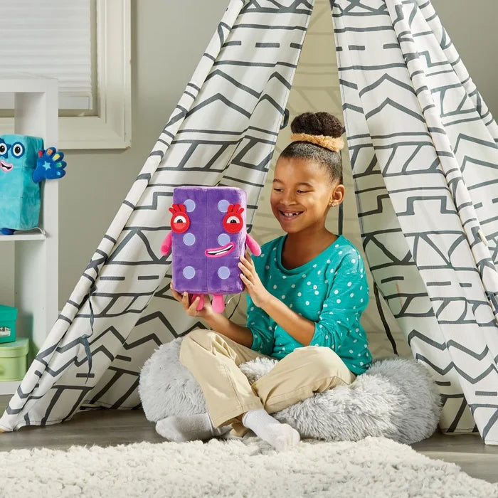 Purple rectangular plush toy with white dots, big red eyes, and pink limbs held by a child in a play tent.