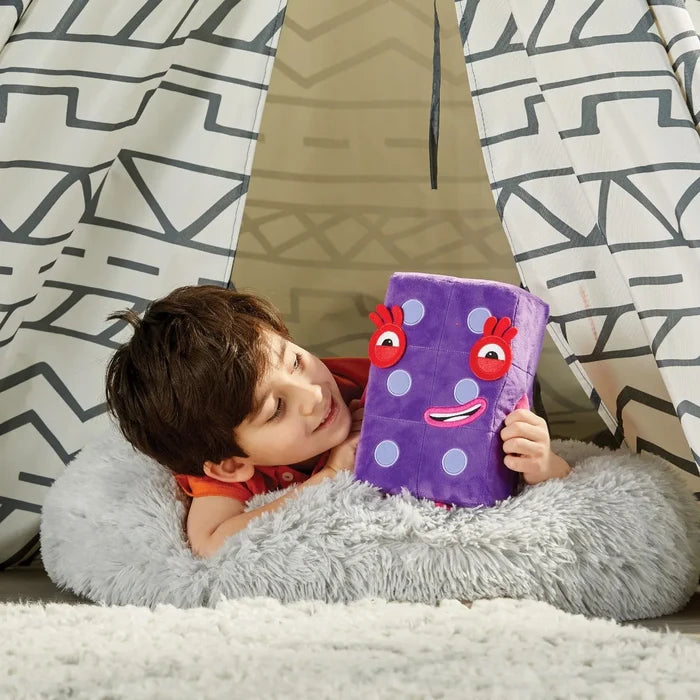 Child holding a purple rectangular plush toy with six dots and a smiling face inside a patterned play teepee.
