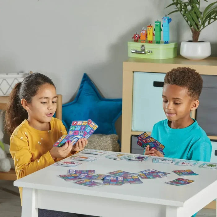 Two children play with colorful Numberblocks character cards featuring bright grid designs on a white play table.