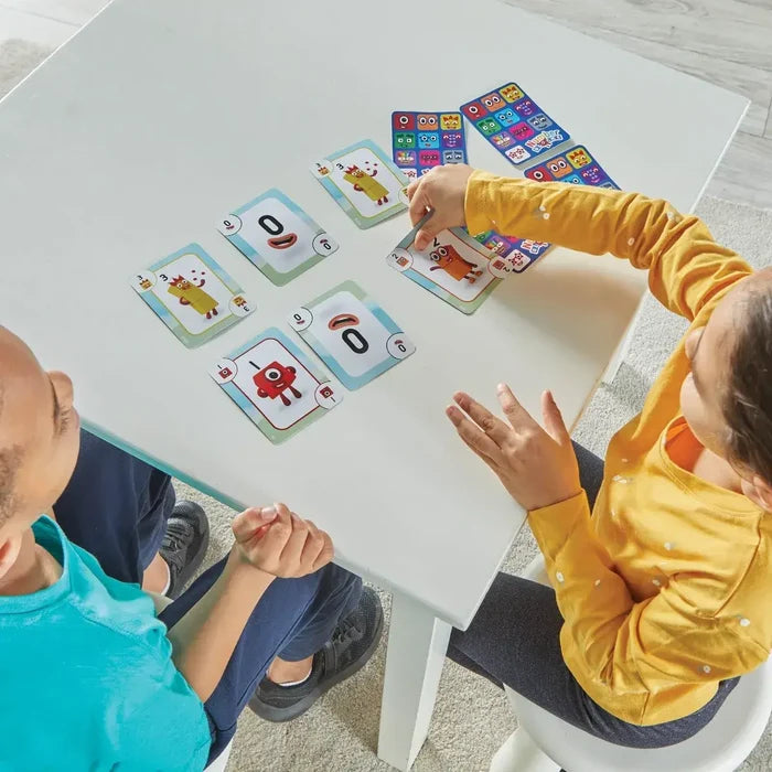 Two children play with colorful Numberblocks cards featuring character art and numbers on a white table.