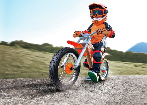 Child in orange safety gear riding a wooden off-road balance bike with large treaded tires on a dirt path.