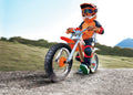 Child in orange safety gear riding a wooden off-road balance bike with large treaded tires on a dirt path.