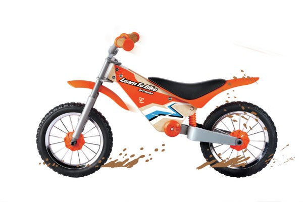 Orange and wood balance bike with dirt bike styling, chunky tires, and Learn To Bike graphics on the frame.