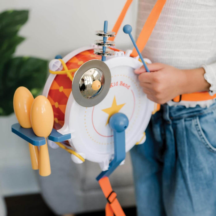 A child wearing a white and orange toy drum with attached yellow maracas, cymbals, and blue drumsticks.